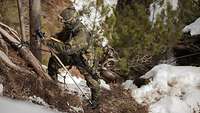 Ein Soldat klettert an einem Seil den verschneiten Waldhang hoch.