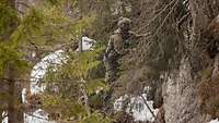 Ein Soldat klettert einen bewachsenen Felsen am Seil bei Schnee hoch.