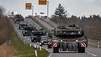 Auf einer Landstraße fahren mehrere militärische Fahrzeuge hintereinander.