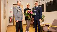 Kamilla Senjo steht zwischen zwei Soldaten mit einem großen Blumenstrauß.