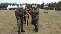 Vier Soldaten halten gemeinsam eine Deutschlandfahne, im Hintergrund sind Soldatinnen und Soldaten angetreten.