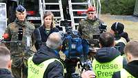 Eine Frau und zwei Soldaten stehen gemeinsam vor der Presse und werden interviewt.