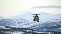 Ein Hubschrauber fliegt vor einer bergigen Winterlandschaft.