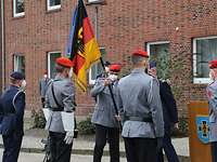 Zwei Soldaten übergeben sich eine Flagge, weitere Soldaten sind angetreten zu sehen.