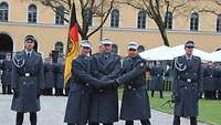 Drei Soldaten stehen vor einer schwarz-rot-goldenen Fahne und reichen sich die Hände.