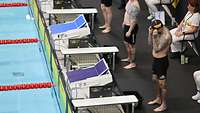 Ein deutscher Schwimmsportler steht vor einem Startblock und richtet seine Schwimmbrille.