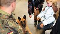 Ein Diensthund liegt bei seinem Hundeführer und wird von Kindern gestreichelt. 