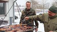 Zwei Soldaten grillen Würstchen und Steaks auf einem Schwenkgrill 
