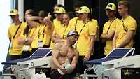 Hinter den Startblöcken im Schwimmbad stehen in gelb gekleidete freiwillige Helfer
