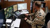 Ein Soldat sitzt an einem Arbeitsplatz und schaut auf seine Monitore