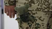Ein grüner Teddybär, der in einer Beintasche eines Soldaten verstaut ist