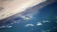 Ein Foto aus einem Flugzeug heraus zeigt ein Schiff an einer Küste liegend.