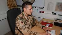 Ein Soldat sitzt an einem Schreibtisch und arbeitet am Computer