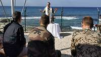 Ein Militärgeistlicher hält eine Messe ab. Im Hintergrund ist das Meer
