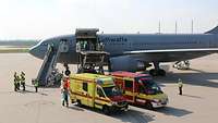 Der Airbus A310 ist auf einem Rollfeld. Zwei Krankenwagen und Personal steht bereit davor und wartet auf die Patienten.
