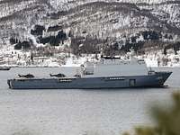 Ein graues Schiff liegt in einem Fjord.