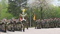 Soldaten in Paradeaufstellung marschieren mit Truppenfahne feierlich ein.