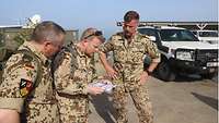 Drei Soldaten stehen im Freien und blicken auf ein Blatt Papier, das der in der Mitte stehende Soldat in der Hand hält