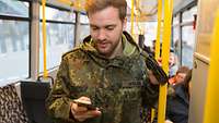 Ein Soldat hält sich mit einer Hand in einer Straßenbahn in Berlin fest und hält in der anderen Hand sein Handy