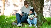 Ein Mann und ein Kind sitzen an einem Baum und lesen ein Buch