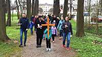 Ein Kind führt mit einem Holzkreuz den Kreuzweg an