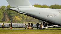 Aus der geöffneten Heckklappe eines Flugzeuges steigen Soldaten mit Hunden aus.