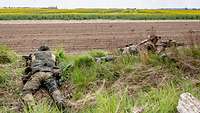Zwei Soldaten liegen mit Waffe im Anschlag im Gras am Feldrand. 