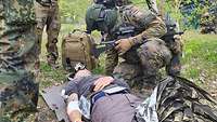 Mehrere Soldaten stehen um eine verletzte zivile Person