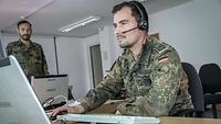 Soldat sitzt hinter einem Schreibtisch an einem Laptop.