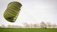 Ein Soldat landet mit seinem grünen Fallschirm auf einem Feld.