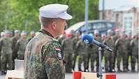 Ein Soldat mit heller Gebirgsmütze steht an einem Rednerpult mit Mikrofon. Vor ihm stehen Soldaten.