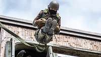 Ein angeleinter Soldat springt aus einem hölzernen Sprungturm.