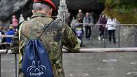 Ein Soldat mit einem Lourdes-Rucksack beim Gottesdienst an der Grotte in Lourdes