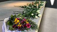 Blumengestecke und weiße Rosen zur Erinnerung an die Gefallenen und Verstorbenen