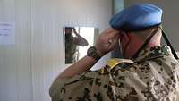 Ein Bundeswehrsoldat von hinten, der in einen Spiegel schaut und ein hellblaues Barett auf seinem Kopf richtet