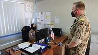 Eine südostasiatische Soldatin mit Kopftuch sitzt an einem Schreibtisch und spricht mit einem deutschen Soldaten