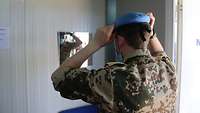 Ein Soldat probiert ein hellblaues Barett an und betrachtet sich dabei im Spiegel