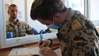 Hinter einem Tresen blickt ein österreichischer Soldat auf einen deutschen, der ein Dokument unterschreibt