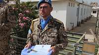 Ein Soldat, der UN-Barett, UN-Halstuch und UN-Patch trägt, hält ein Tablett mit Urkunde und Medaille vor sich