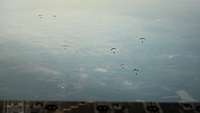 Zahlreiche Fallschirme schweben am grauen Horizont.
