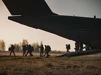 Mehrere Soldaten steigen im Morgengrauen aus der Heckrampe eines großen Flugzeuges.