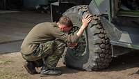 Ein Soldat hockt vor dem Reifen eines Fahrzeugs