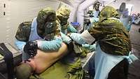 Mehrere Soldaten in Schutzanzügen verpflegen im Zuge einer Übung einen verwundeten Soldaten in einem aufblasbaren Zelt.