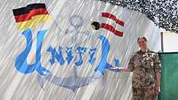 Michelle P. steht neben einer Wand, auf die sie den Schriftzug UNIFIL, einen Anker und die zwei Flaggen gemalt hat