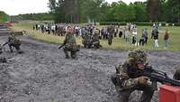 Bewaffnete Soldaten knien im Sand zwischen zwei Hindernissen und sichern die Umgebung.