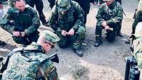 Ein Soldat zeigt mit einem Stift etwas auf einem Klemmbrett, andere Soldaten schauen zu