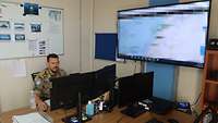 Ein Soldat sitzt an einem Schreibtisch vor zwei Monitoren. Rechts hängt ein Großbildschirm mit einer Lagekarte des Libanons.