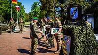 Auf einem Platz stehen Soldaten nebeneinander, zwei Soldaten vor ihnen überreichen Urkunden.