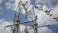 Von langen Leinen an den Mastenn zweier Segelschiffe wehen bunte Signalflaggen.