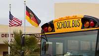 Ein gelber Schulbus und die amerikanische sowie die deutsch Flagge.